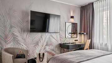 Een moderne hotelkamer met een groot bed, een flatscreen televisie aan de muur, een bureau met stoel, en een groot raam met gordijnen.