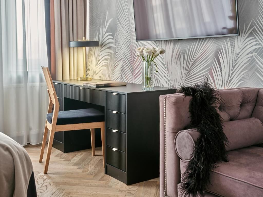 A modern room with a desk, a chair, a sofa, and a flat-screen TV mounted on the wall.