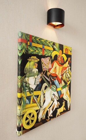 Una obra de arte colgada en la pared que muestra una escena tradicional con un jinete a caballo, sobre un muro con textura.