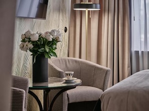 Une chambre d’hôtel avec une table ronde en verre, un vase de fleurs, un téléviseur fixé au mur et une lampe.