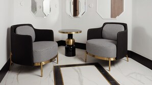 Une pièce comprenant deux fauteuils à motifs noir et blanc, une table ronde avec un pied noir et de nombreux miroirs hexagonaux accrochés aux murs.