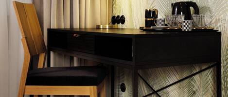 Una habitación moderna con un escritorio de madera, una silla, una lámpara y una pared con estampado de hojas de palma.