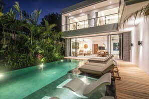Ein modernes, zweistöckiges Haus mit Swimmingpool, Außenbereich zum Sitzen und einem gut beleuchteten Innenraum.