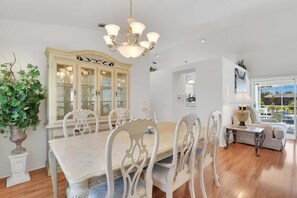 Ein Esszimmer mit großem Tisch, weißen Stühlen, einer Glasschrank und einem Kronleuchter.