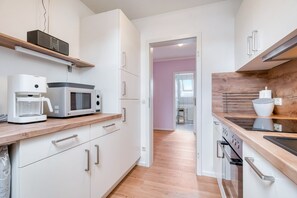 Une cuisine moderne avec des meubles blancs, un four à micro-ondes, une machine à café et des plans de travail en bois.