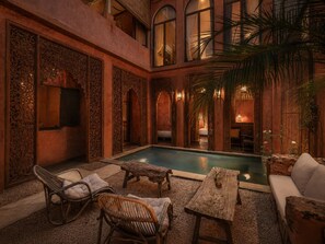 Uma área de piscina interna com mesa de madeira, cadeiras de vime e um sofá.