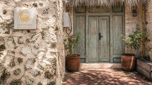 Un mur de pierres rustiques, une enseigne indiquant « The Rose Moon Boutique Villa », une porte en bois et deux plantes en pot.