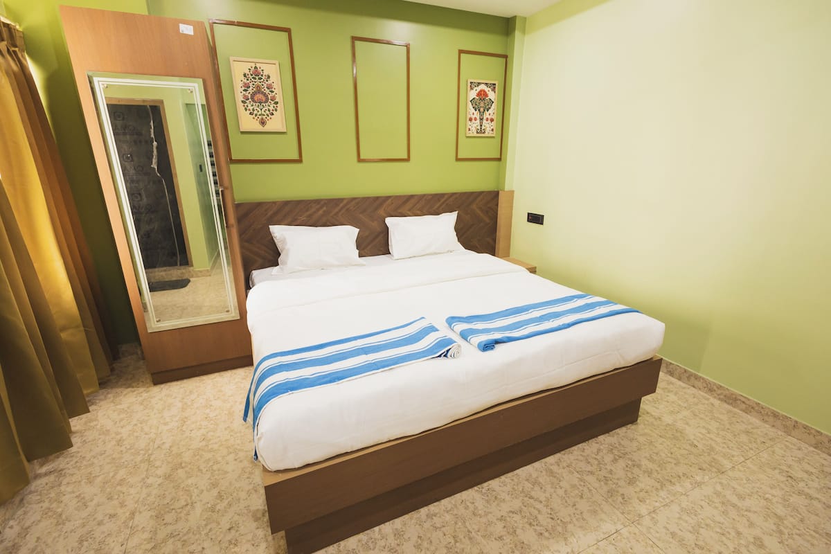 A neatly made bed with white and blue striped bedding in a room with green walls and a wooden headboard.