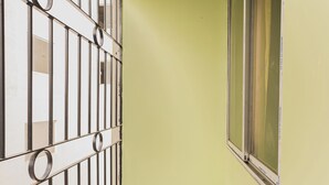 A narrow hallway with a barred window and a door, a tiled floor, and a green wall. - Lotus Leaf Guest House (Guwahati)