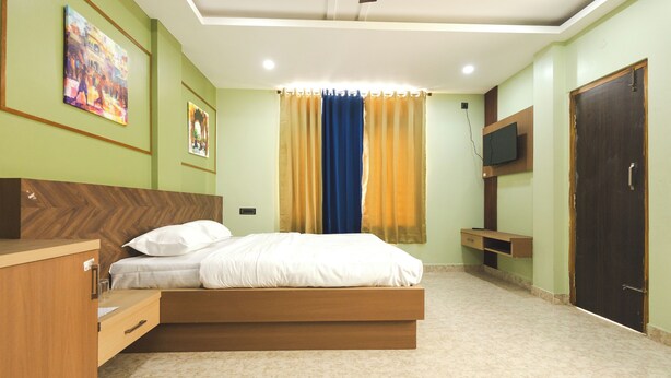 A bedroom with a bed, a wooden dresser, a TV, and a door. - Lotus Leaf Guest House (Guwahati)