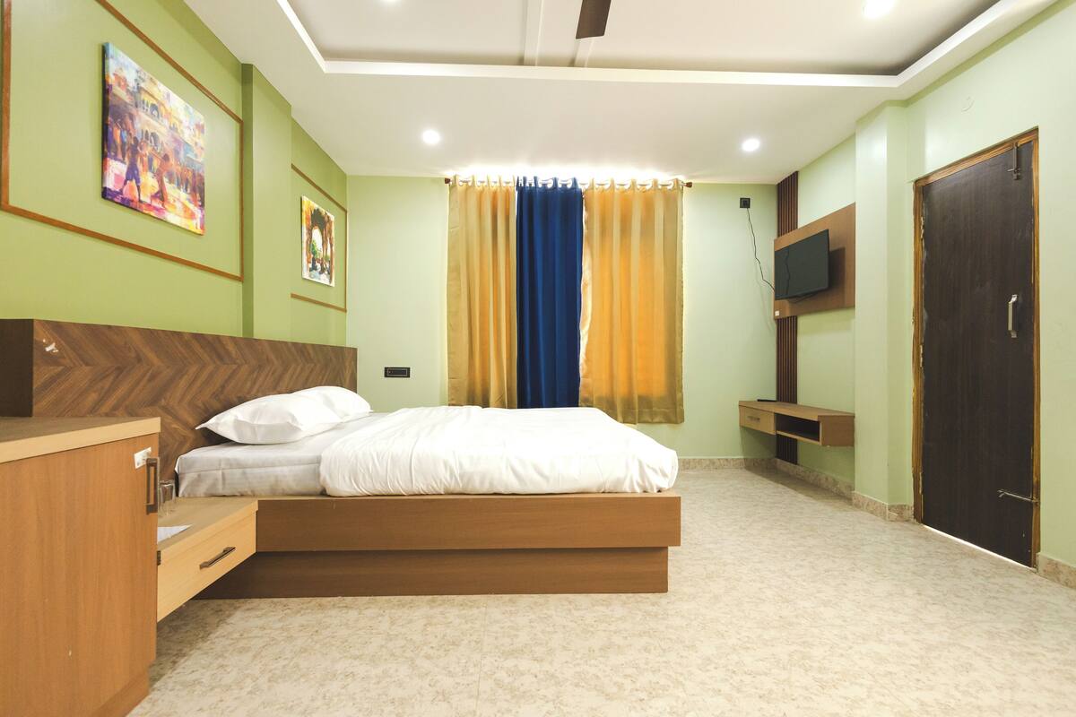 A bedroom with a bed, a wooden dresser, a TV, and a door.