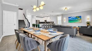 A modern dining area with a wooden table set for six, grey upholstered chairs, and pendant lighting. - Luxury Incredible Themed Home, best vacation (Kissimmee)