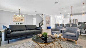 A modern living room with a sofa, armchairs, and a coffee table. There is a staircase leading to another level. - Luxury Incredible Themed Home, best vacation (Kissimmee)
