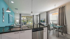 Una cocina moderna con una isla central, electrodomésticos de acero inoxidable y un comedor con mesa y sillas de vidrio.