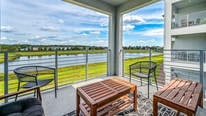 A balcony with a view of a lake, two wooden tables, and two chairs. - Spacious, Beautiful 3-BR Condo, Prime Location (Kissimmee)