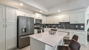 A modern kitchen with white cabinets, stainless steel appliances, and a central island with seating. - Spacious, Beautiful 3-BR Condo, Prime Location (Kissimmee)