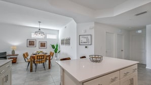 A modern kitchen with a central island, dining area with chairs, and a hanging light fixture. - Spacious, Beautiful 3-BR Condo, Prime Location (Kissimmee)