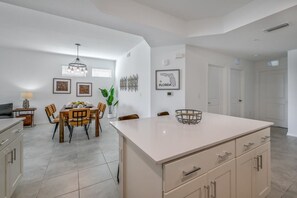 A modern kitchen with a central island, dining area with chairs, and a hanging light fixture. - Spacious, Beautiful 3-BR Condo, Prime Location (Kissimmee)