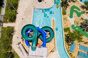 An aerial view of a water park with a large water slide, a pool, and a sandy area with lounge chairs. - Spacious, Beautiful 3-BR Condo, Prime Location (Kissimmee)