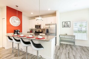 A modern kitchen with a central island, bar stools, a clock, and a dining area with a bench. - Cozy Home in Amazing Resort for Perfect Vacations (Four Corners)