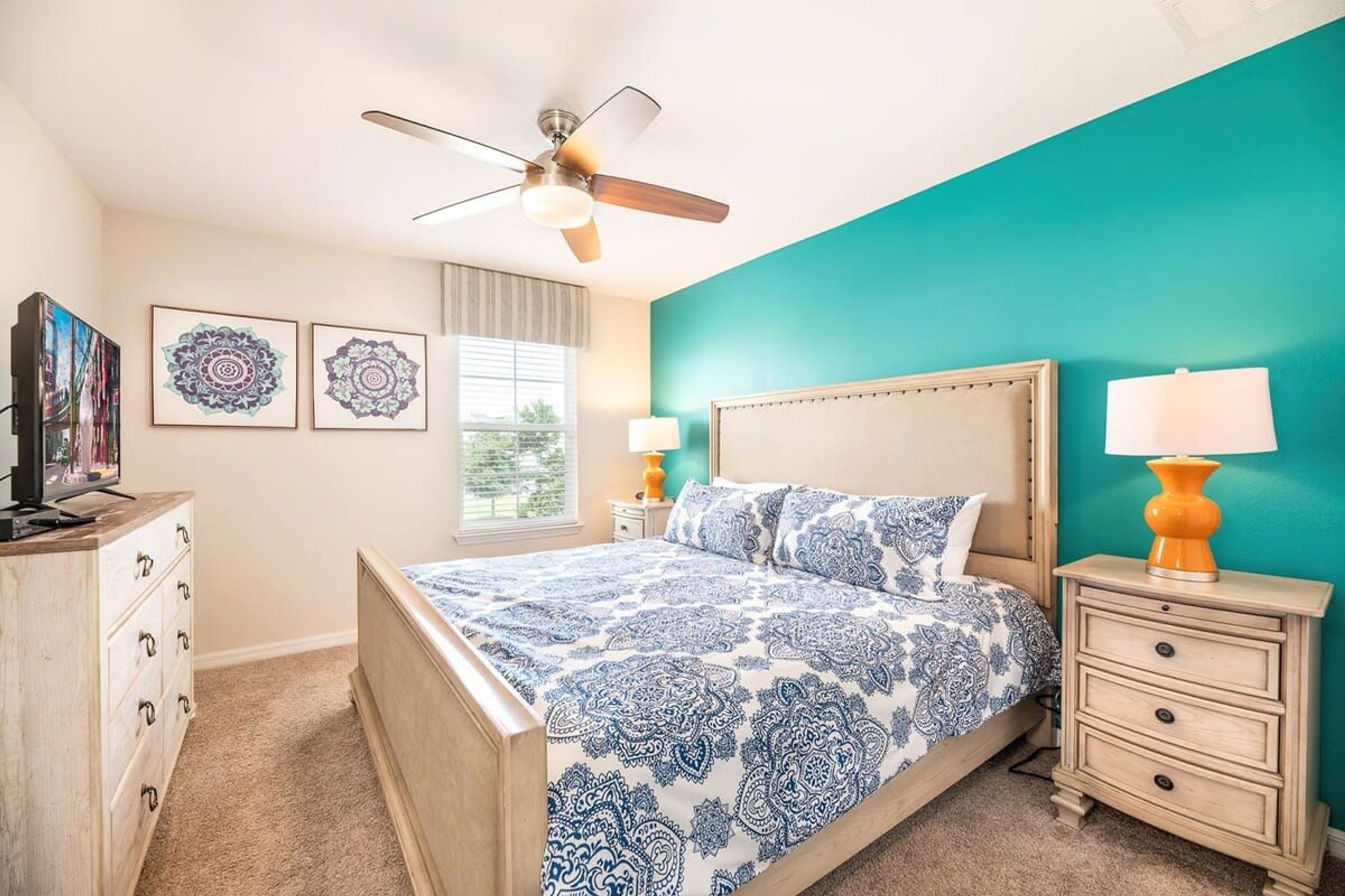 A bedroom with a bed, two bedside tables, a ceiling fan, and a TV on a dresser.