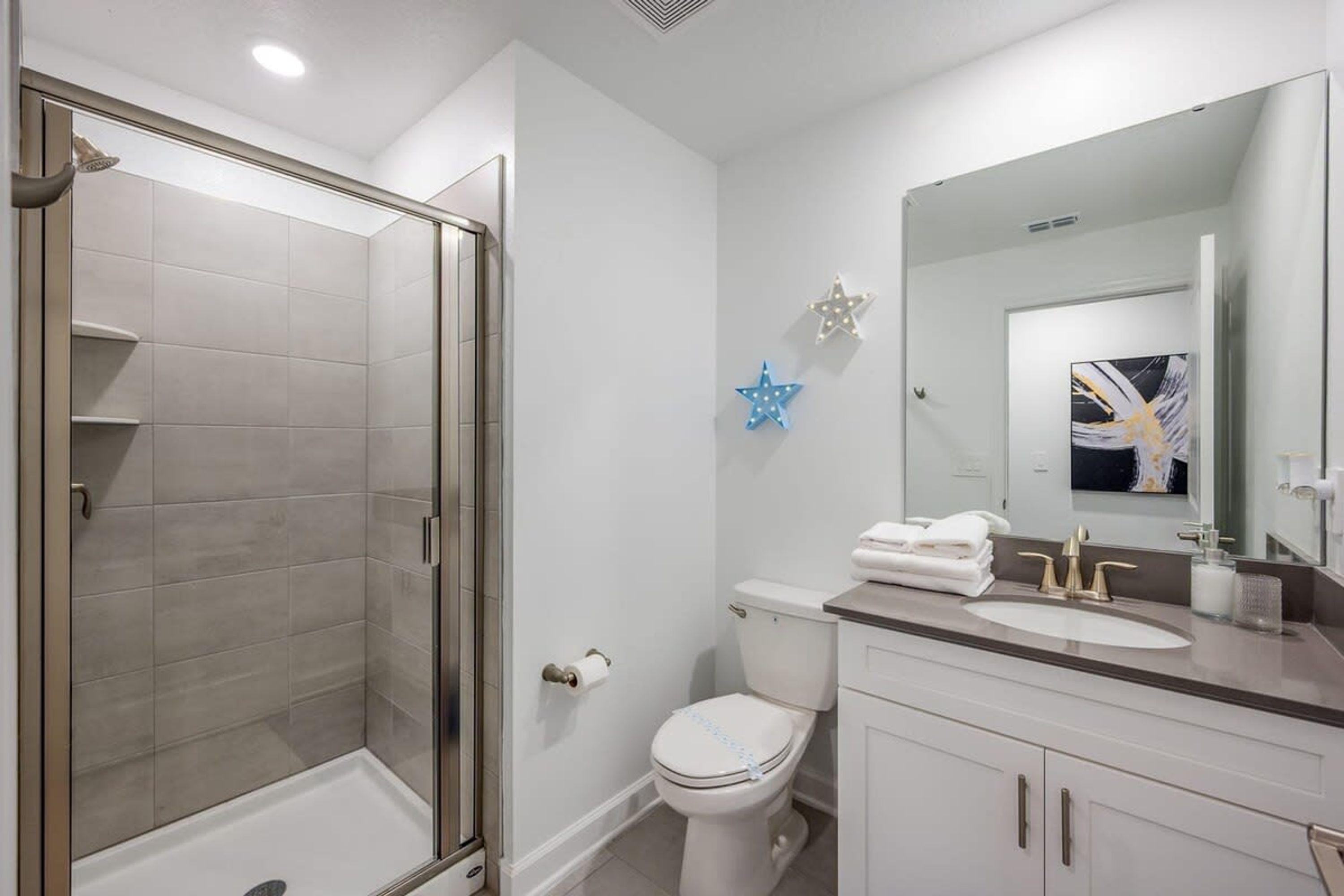 A modern bathroom with a glass-enclosed shower, a toilet, and a sink with a large mirror.