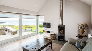 Un salon spacieux avec une grande fenêtre donnant sur la mer, une cheminée, un téléviseur et un coin salon confortable.