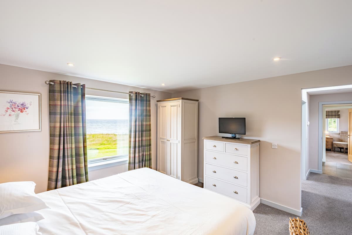 Une chambre à coucher avec un lit, une commode, une télévision et une vue sur la mer.
