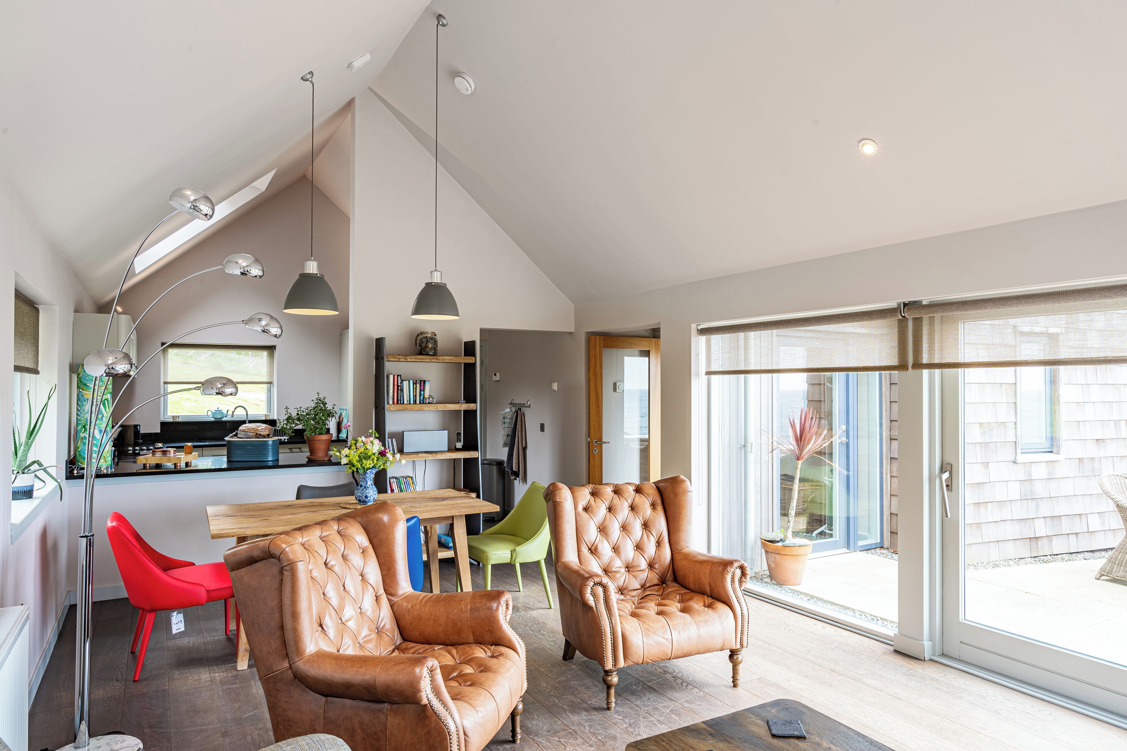 A spacious living area with leather armchairs, a dining table, and a kitchen in the background.