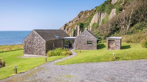 Une maison située sur la côte, avec une allée en gravier, un petit abri de jardin et une vue sur la mer.