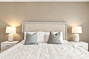 A neatly made bed with a textured white duvet, two grey pillows, and a headboard with a beaded trim. - Premium 5-Bed Townhome, Themed, Perfect Location (Four Corners)