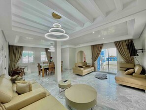 Ein geräumiges Wohnzimmer mit Essbereich, einer Sofagarnitur, einem runden Couchtisch und einer Chandelier.