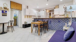 Una cocina moderna con armarios blancos, un comedor con mesa y sillas de madera, y un sofá púrpura.