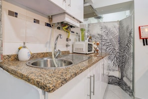 A kitchen with a granite countertop, stainless steel sink, and a microwave. - Family House in the Heart of Aveiro (Aveiro)
