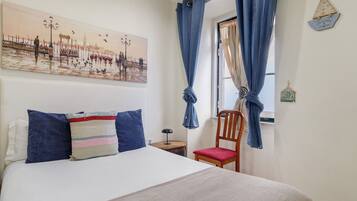 A bedroom with a bed, a chair, a nightstand, a painting, and a window with curtains.