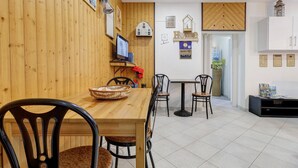 Una habitación con paneles de madera, una mesa de comedor, sillas, un televisor y una pequeña cocina con armarios.