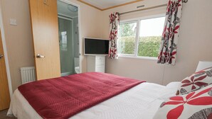 Une chambre à coucher comprenant un lit, une télévision, une fenêtre avec des rideaux et une porte donnant sur une salle de bain.
