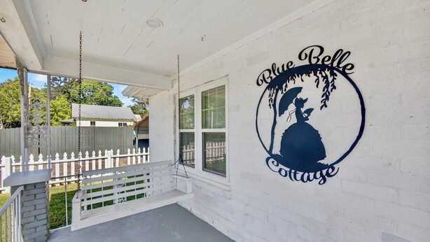 Un porche con una hamaca, cerca blanca y un cartel que dice 'Blue Belle Cottage'.