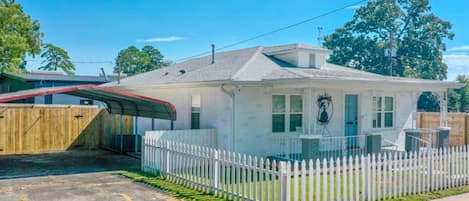 A single-story house with a white exterior, a covered porch, and a fenced yard.