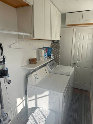 A compact laundry room with a front-loading washer and dryer, a drying rack, and a small shelf with laundry supplies. - 2 bedrooms king/queen, sofa bed, fenced yard (Aiken)