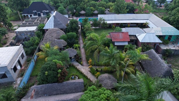 A residential area with multiple houses, some with thatched roofs, surrounded by lush greenery and palm trees. - APAO VILLAGE & RESORT LODGE (Dar es Salaam)