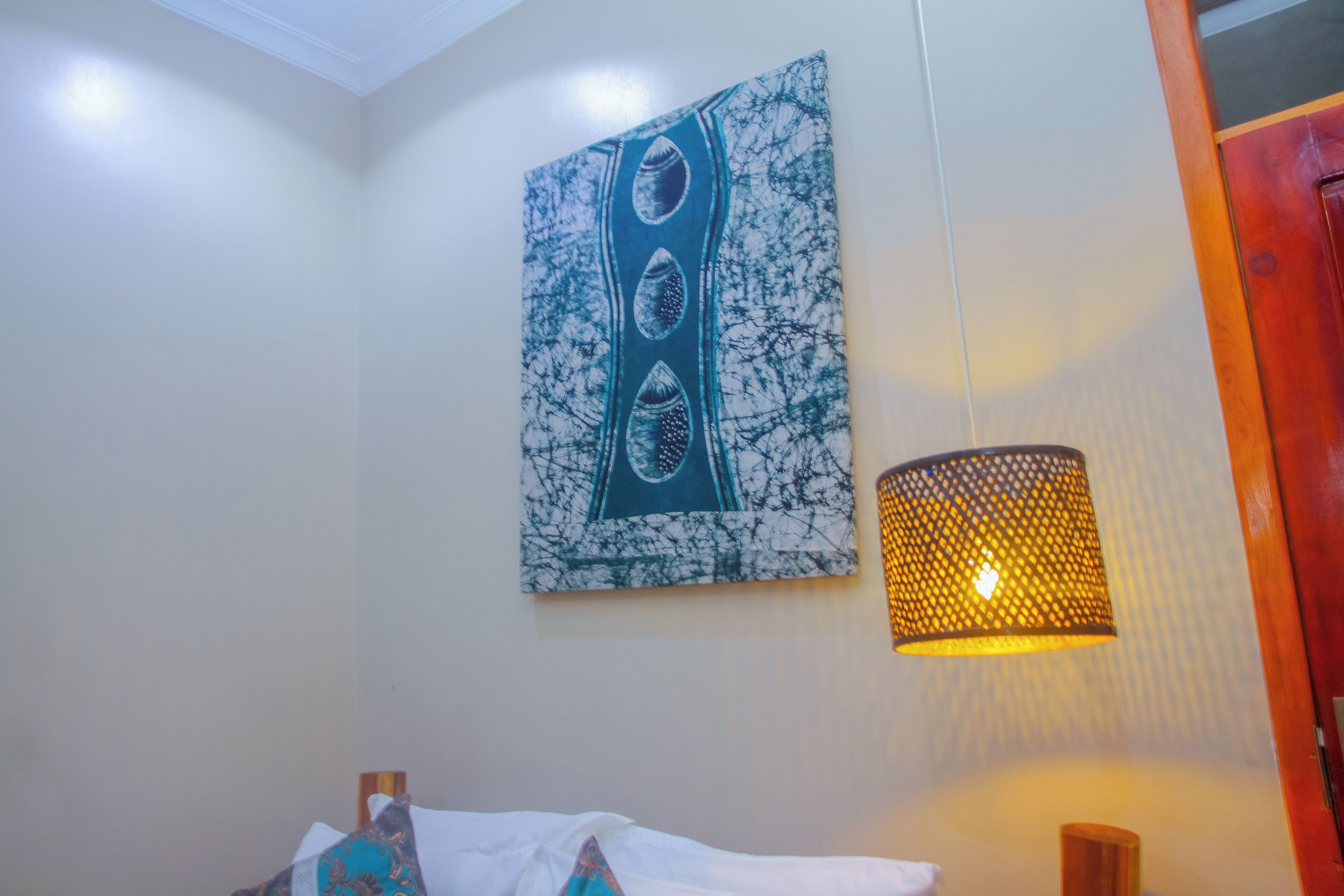 A room with a bed, a wall-mounted painting, and a hanging lamp.