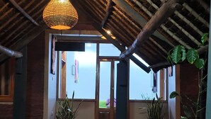 A covered outdoor area with a thatched roof, potted plants, and a tiled floor leading to a door. - APAO VILLAGE & RESORT LODGE (Dar es Salaam)