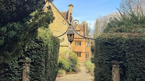 Un bâtiment en pierre, auquel mène un chemin de gravier, entouré d’une végétation luxuriante.
