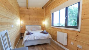 Une pièce de cabane en bois comprenant un lit, une chaise, une fenêtre et un radiateur.