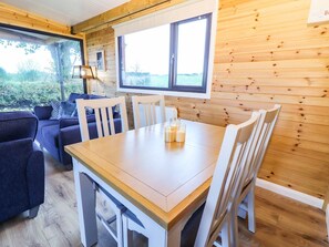 Ein gemütliches Blockhaus-Interieur mit einem Holztisch, weißen Stühlen, einer Couch und einem großen Fenster mit Blick auf Grünflächen.