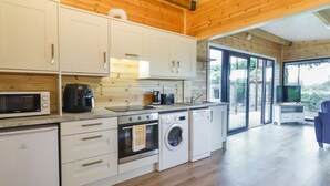 Une cuisine moderne avec des murs en bois, des armoires blanches, un four à micro-ondes, une machine à café, un évier, une cuisinière et un lave-linge.