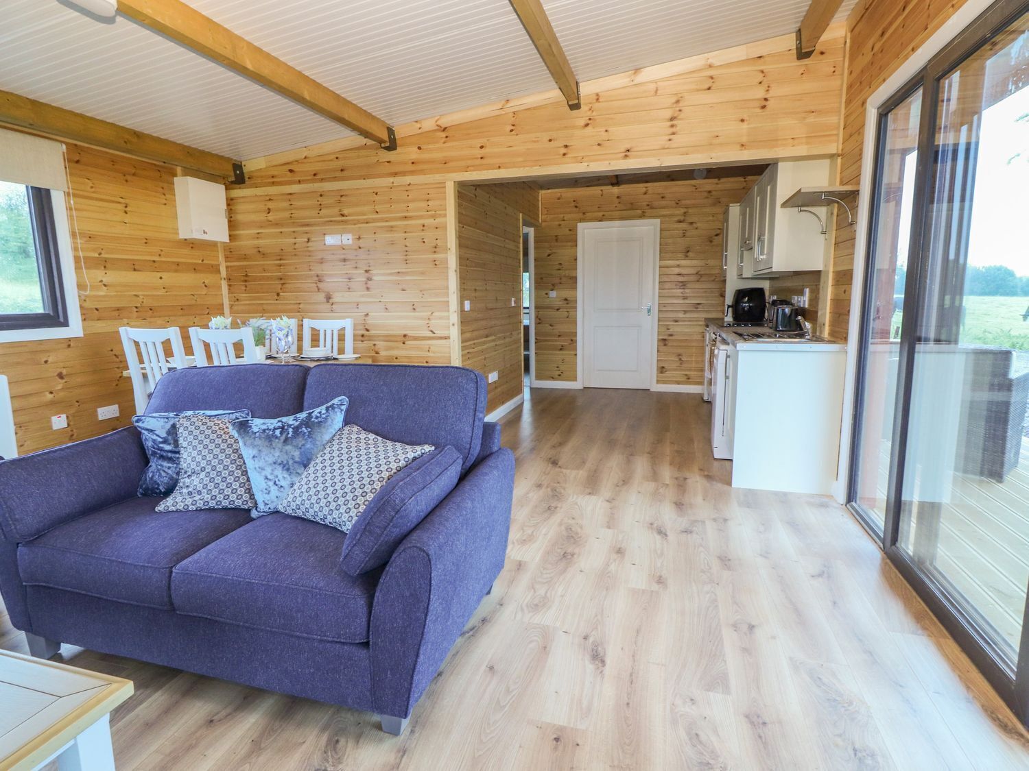 A modern log cabin interior with a sofa, dining area, kitchen, and large windows.