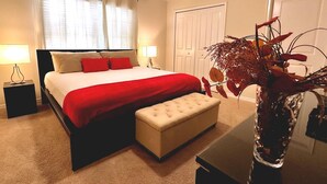 A hotel room with a bed, bedside lamps, a bench, a vase with dried flowers, and a door. - 4Bed Home in Storey Lake with Private Pool (Kissimmee)