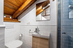 A bathroom with a white toilet, a sink with a mirror above it, and a shower area. - Chalet 'Las Casillas' with Private Terrace, Wi-Fi, and Air Conditioning (Güejar Sierra)